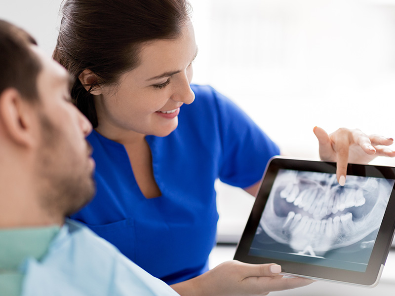 A healthcare professional, possibly a dentist or orthodontist, is showing a patient an image of their teeth on a tablet.