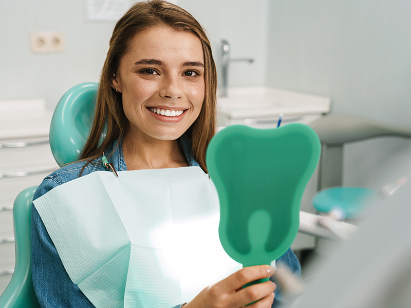 A young woman in a dental office, smiling and holding a green dental impression tray.