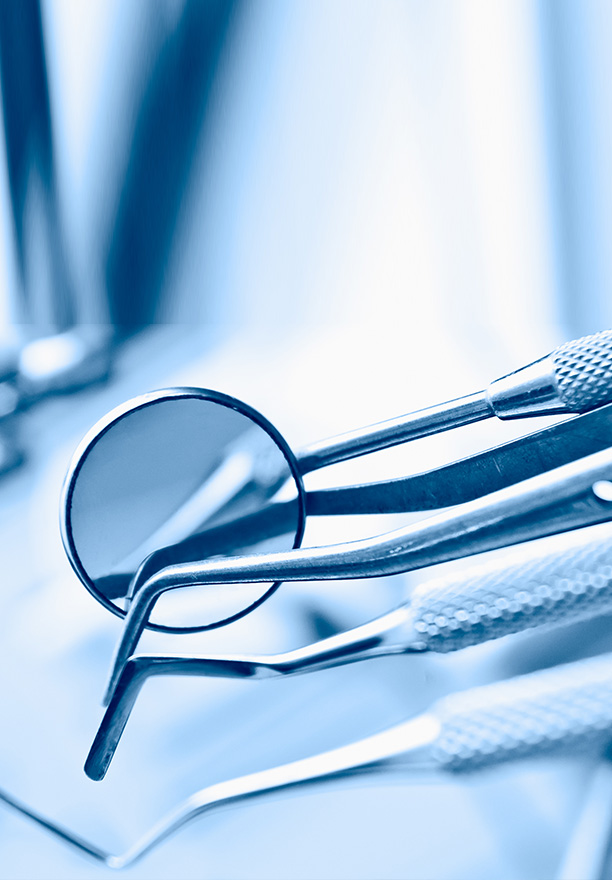 The image shows a pair of metal tweezers with a magnifying glass placed on top, set against the background of a dental office environment filled with various dental instruments and equipment.