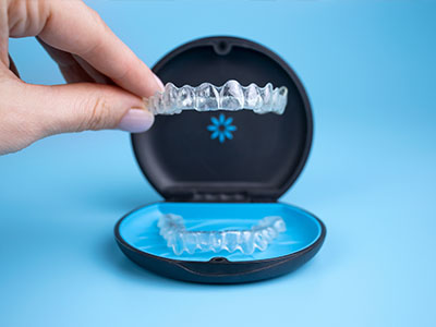 The image shows a person s hand holding an open case containing a set of clear, plastic aligners commonly used for orthodontic treatment.