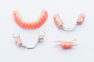 The image shows a collection of dental prosthetics, including a pair of upper dentures with a partial set of lower dentures, displayed against a white background.