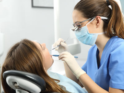 A dental hygienist performing a teeth cleaning on a patient in a dental office setting.