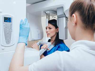 A woman in a blue lab coat standing next to a large, modern 3D scanner, with another person wearing gloves inspecting the equipment.