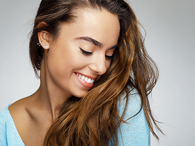 A young woman with long brown hair, smiling and looking down slightly.