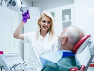 A dental professional assisting an older man in a dental chair, with the professional holding a mirror.