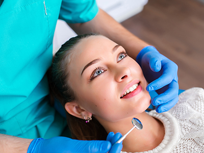 The image shows a dental professional performing a procedure on a patient, with the patient smiling and looking at the camera.
