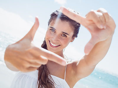 Woman holding up a peace sign with both hands, smiling at the camera, against a bright blue sky background.