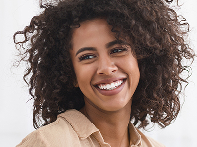 A woman with curly hair and a radiant smile, wearing a beige top, against a white background.